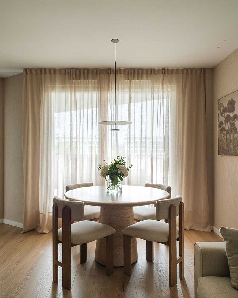 Comedor de Casa Kane junto a un gran ventanal con mesa redonda y sillas tapizadas