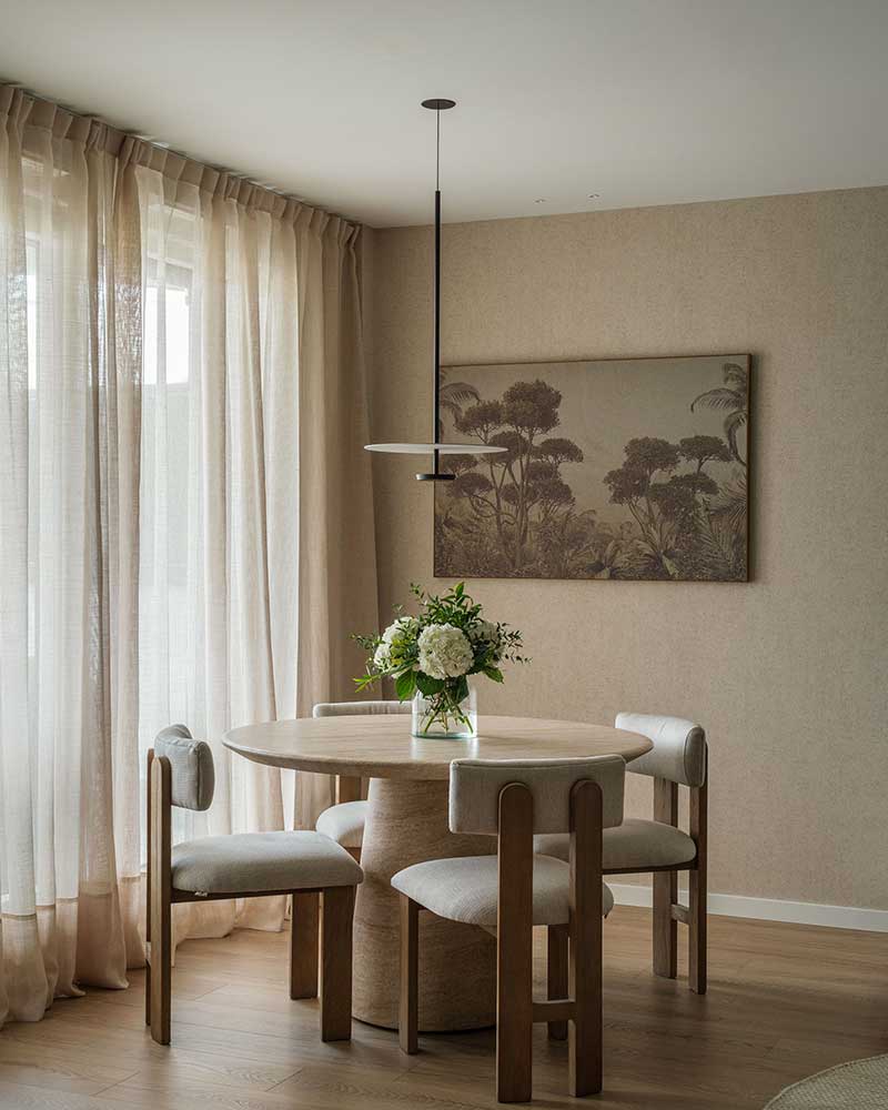 Comedor de Casa Kane con mesa redonda de madera, sillas tapizadas y luz natural