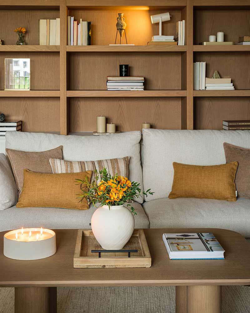 Detalle del salón de Casa Kane con sofá, estantería de madera y decoración en tonos cálidos