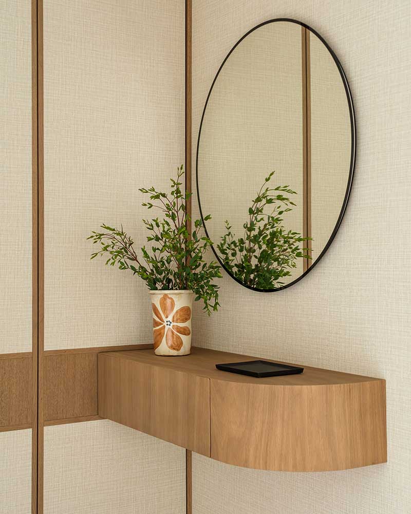 Recibidor de Casa Kane con consola de madera, espejo ovalado y revestimiento textil