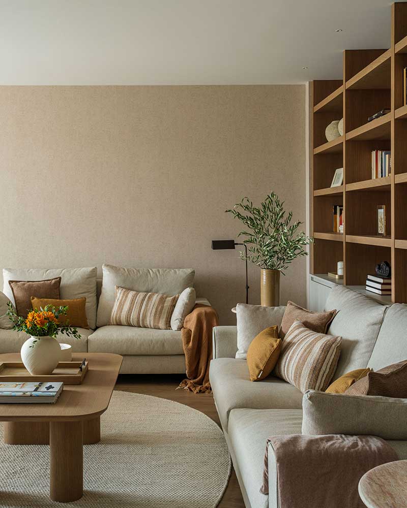 Salón de Casa Kane con sofás en tonos neutros, mesa de madera y estantería integrada